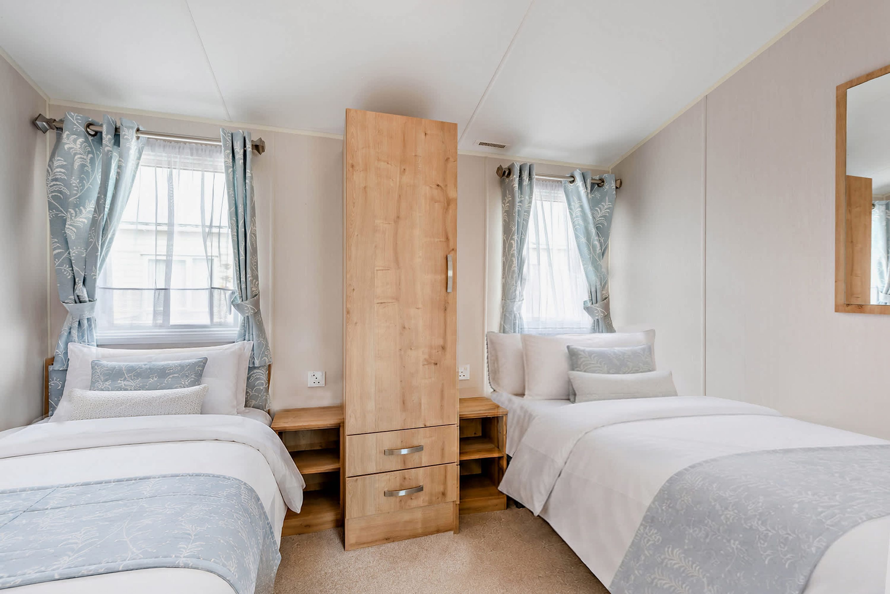 A bedroom with two beds, a wooden wardrobe, and a window with curtains.