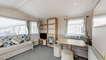 Interior aconchegante de uma motorhome, com sofá, televisão, mesa pequena e cozinha compacta.