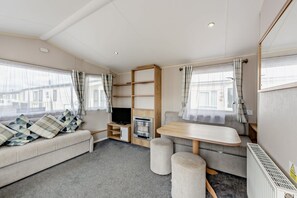 A cozy RV interior with a sofa, a TV, a small table, and a kitchenette area. - Host Stay - Meadow View (Winchelsea)