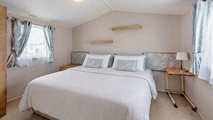 Ein Schlafzimmer mit Bett, Nachttischen, einer Lampe und Vorhängen.