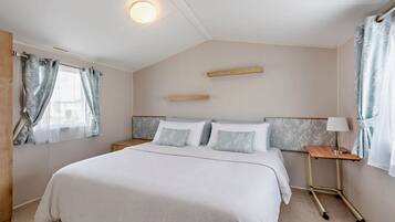 Quarto com cama, mesas de cabeceira, abajur e cortinas.