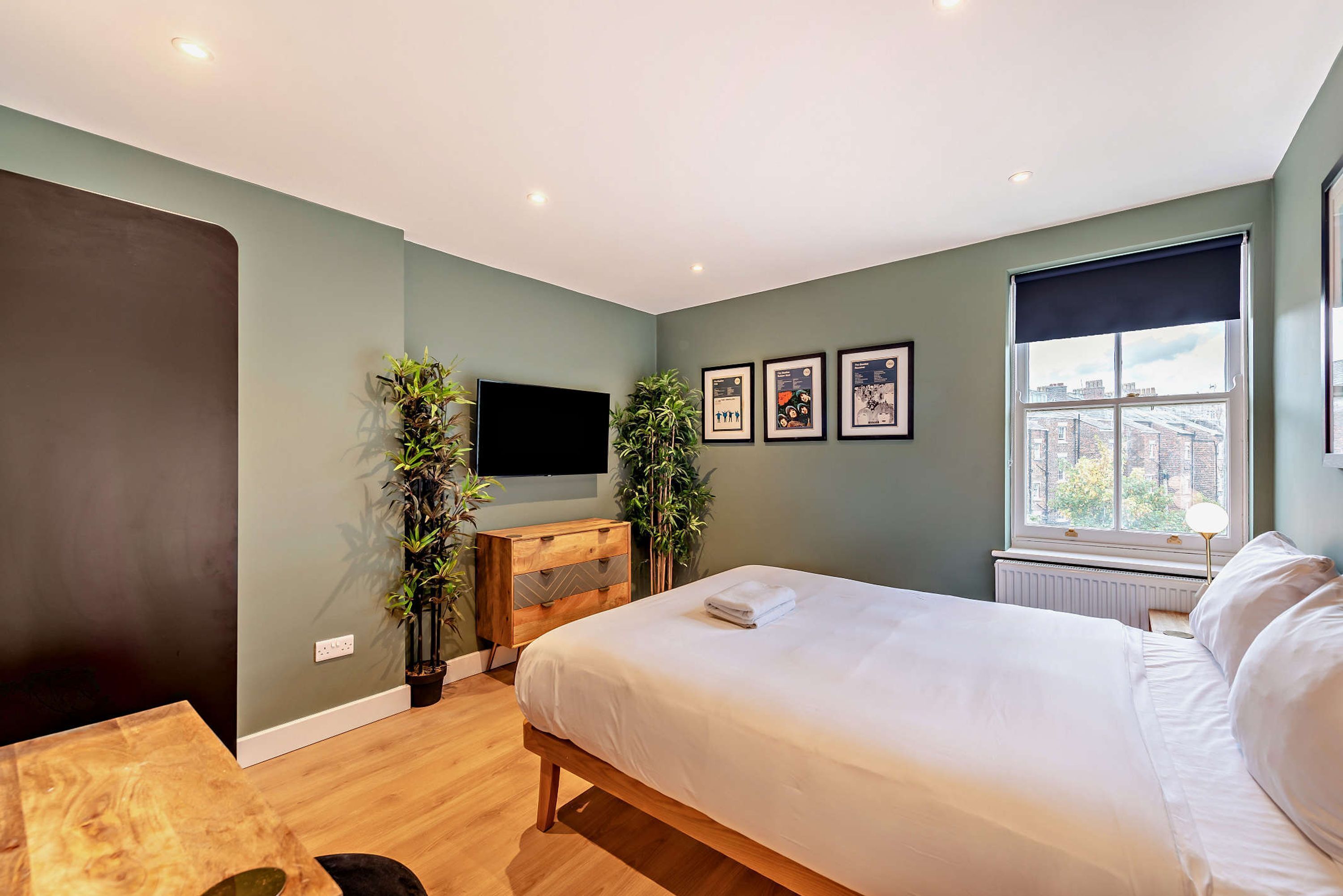 A modern bedroom with a bed, a flat-screen TV, a dresser, and framed pictures on the wall.