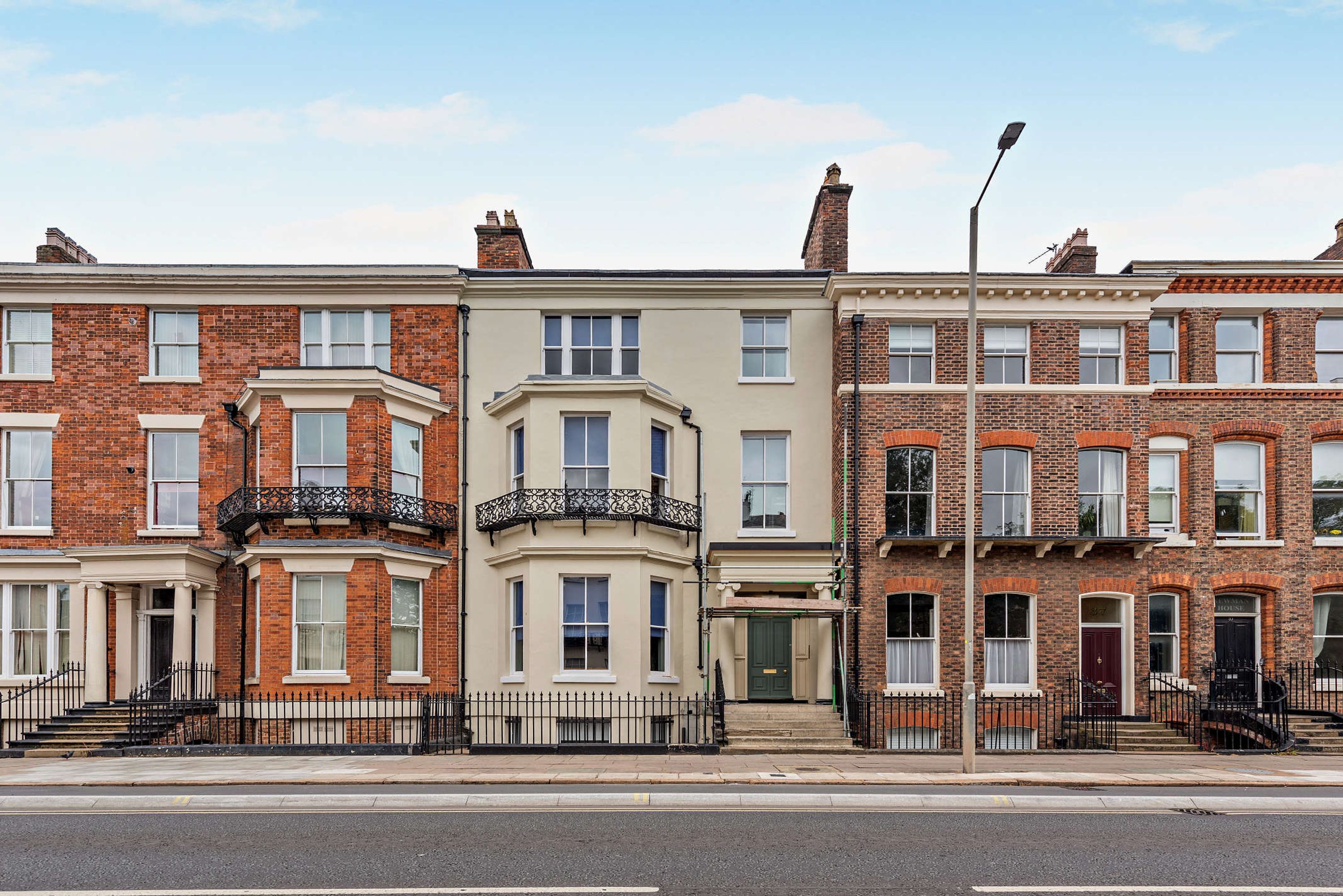 A row of terraced houses with brick facades, white window frames, and black metal railings.