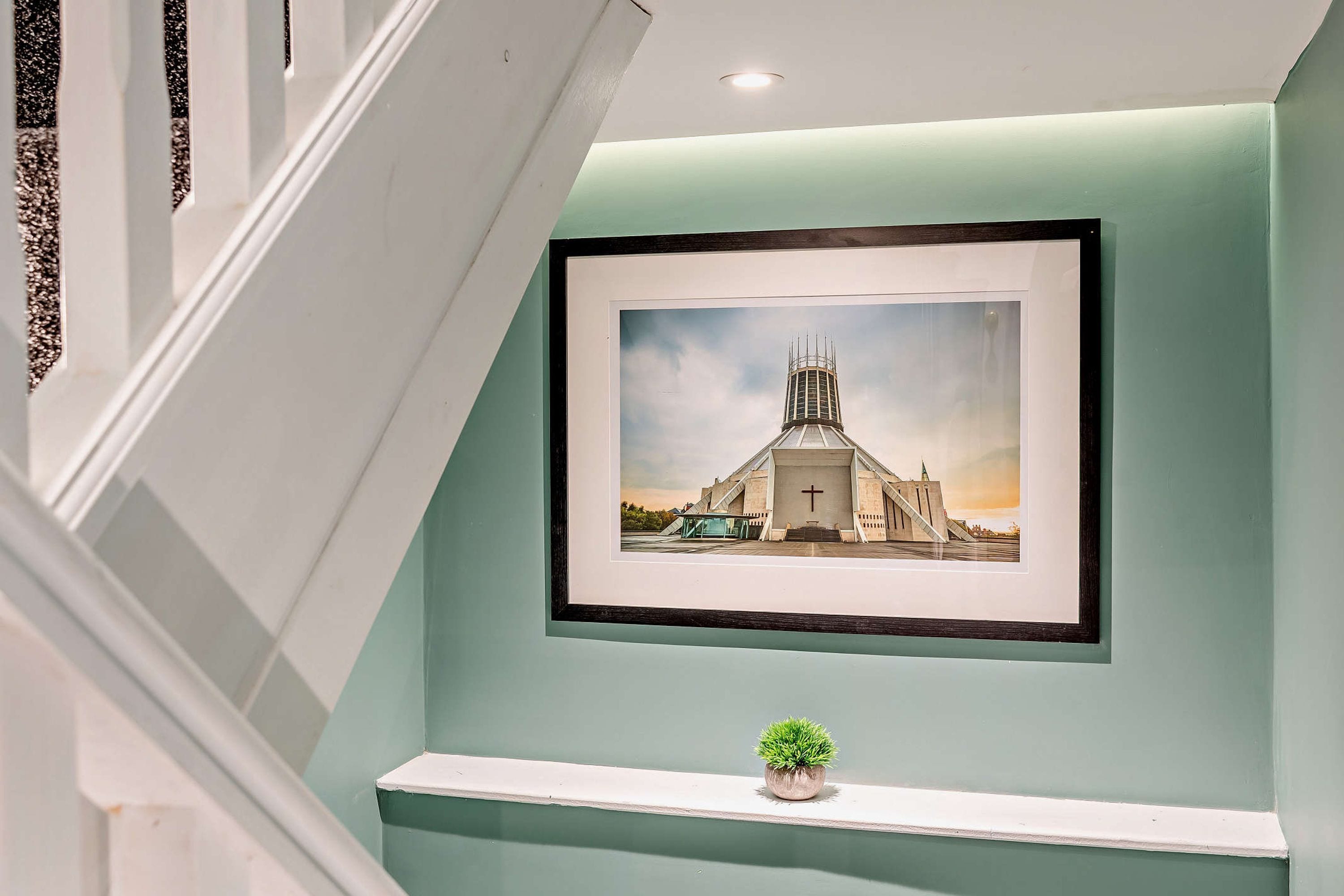 A framed picture of a church on a wall with a small potted plant below it.