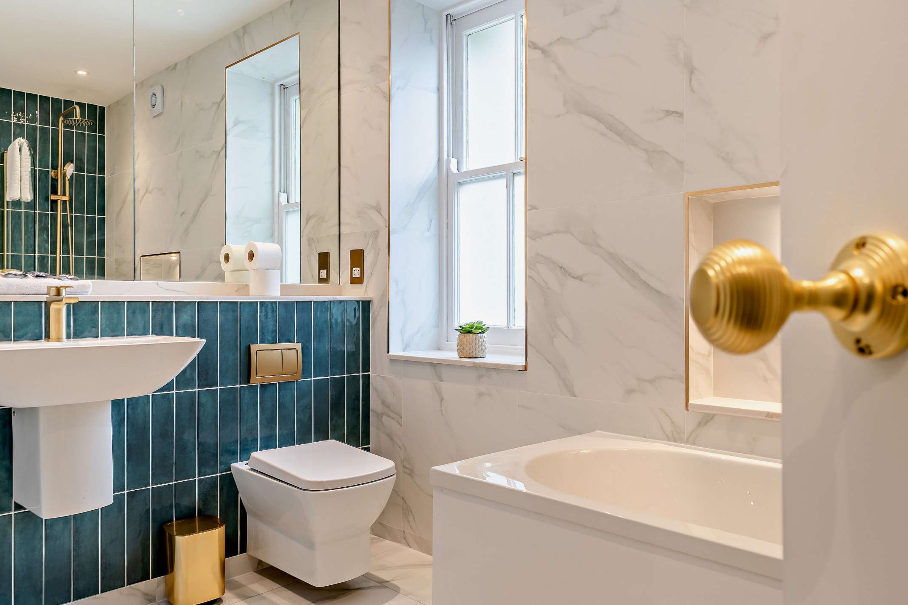 Ein modernes Badezimmer mit einer weißen Badewanne, einer weißen Toilette und einem Waschbecken mit goldenem Wasserhahn.