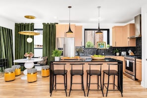 Una cocina moderna con una isla central, taburetes de bar, un refrigerador y una estufa.