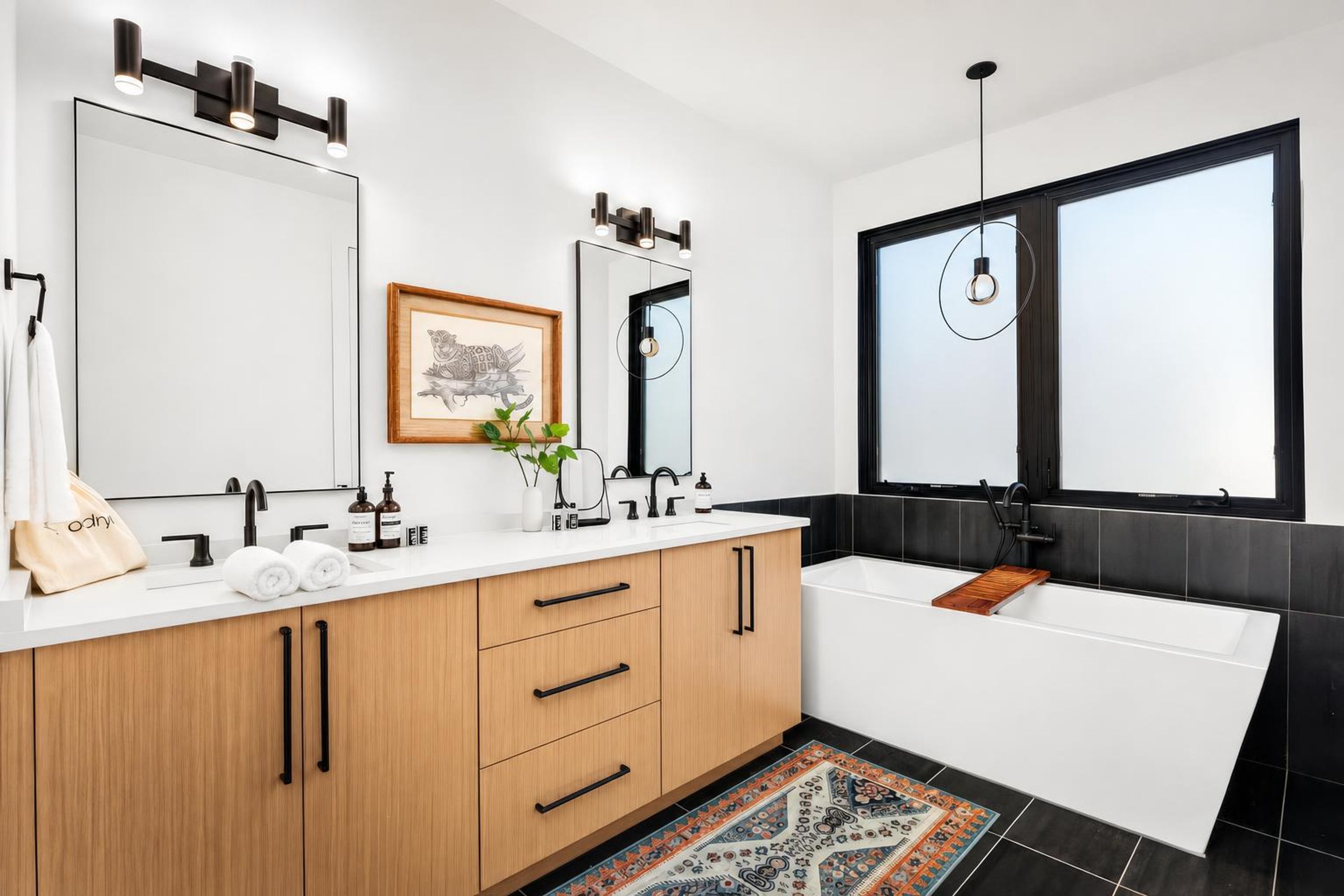 Un bagno moderno con lavabo doppio, un ampio specchio, un'opera d'arte incorniciata e una finestra con lampada a sospensione.