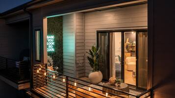 A modern building exterior with a neon sign, a balcony with railings, and a potted plant.