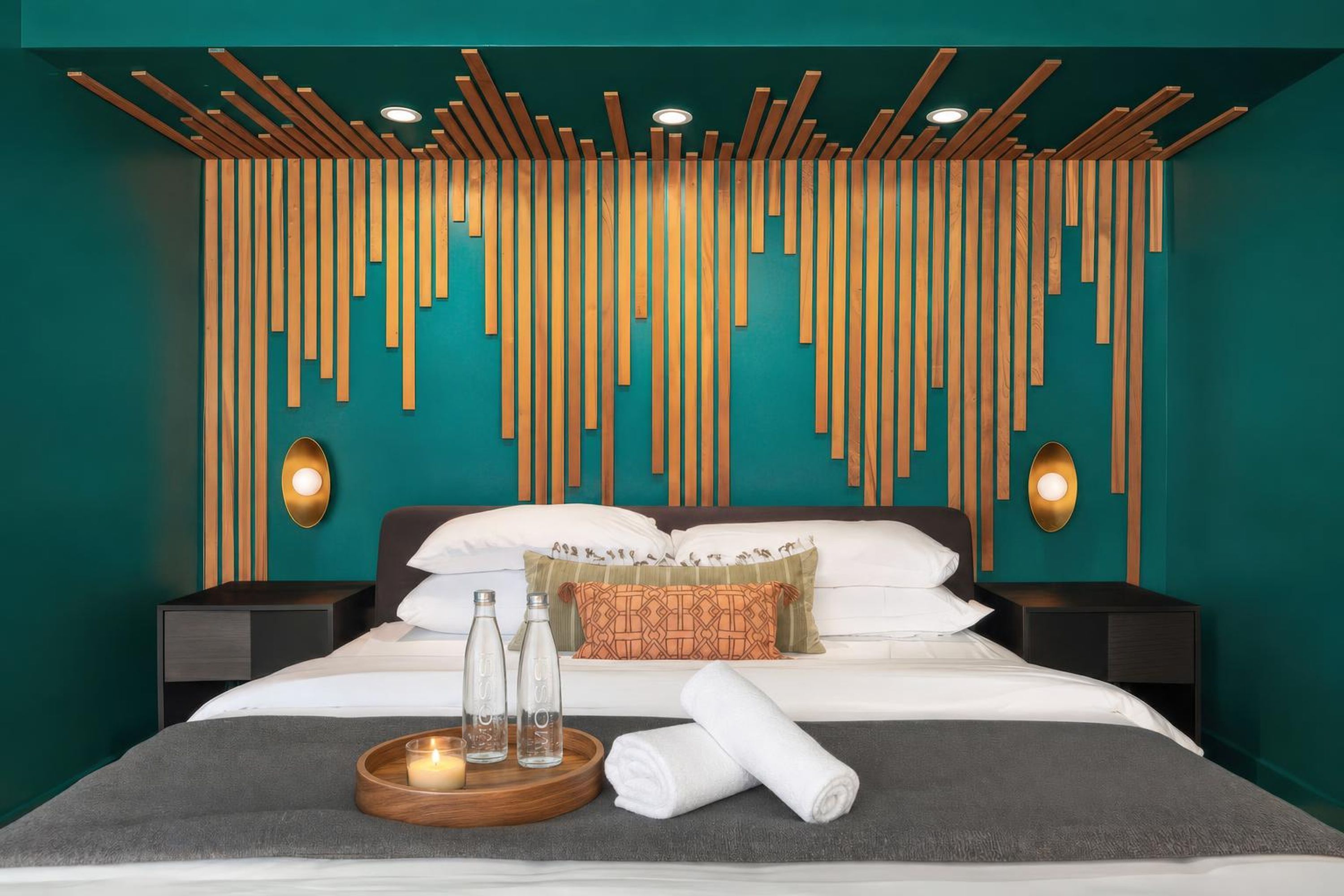 A hotel room with a bed, nightstands, a wall with vertical wooden slats, and two wall-mounted lamps.