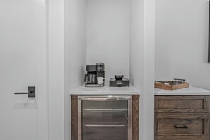 Een kitchenette met een koffiezetapparaat, een kleine koelkast en een houten kastje.