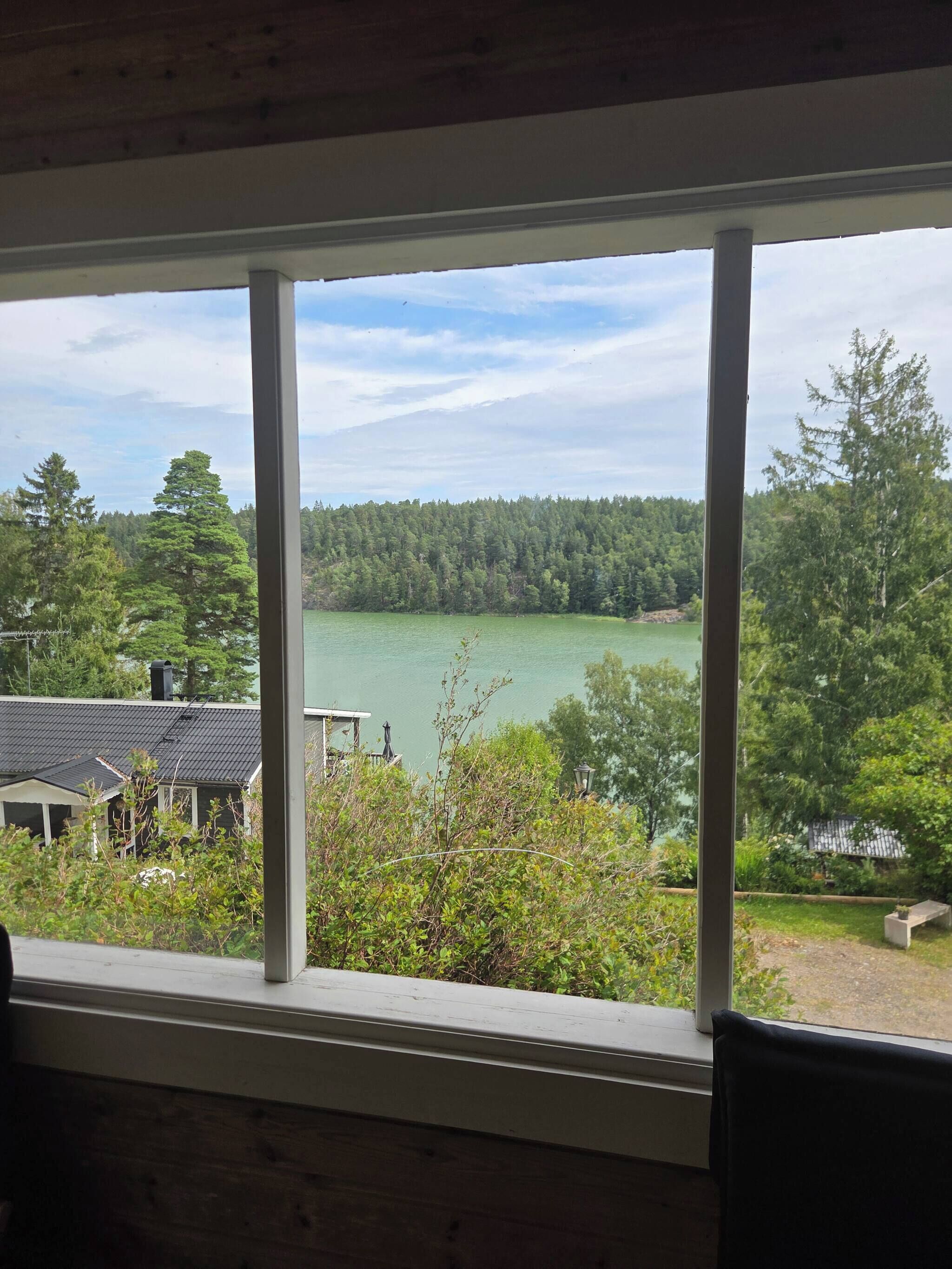 A view from a window overlooking a lake with a forested area and a building with a dark roof.