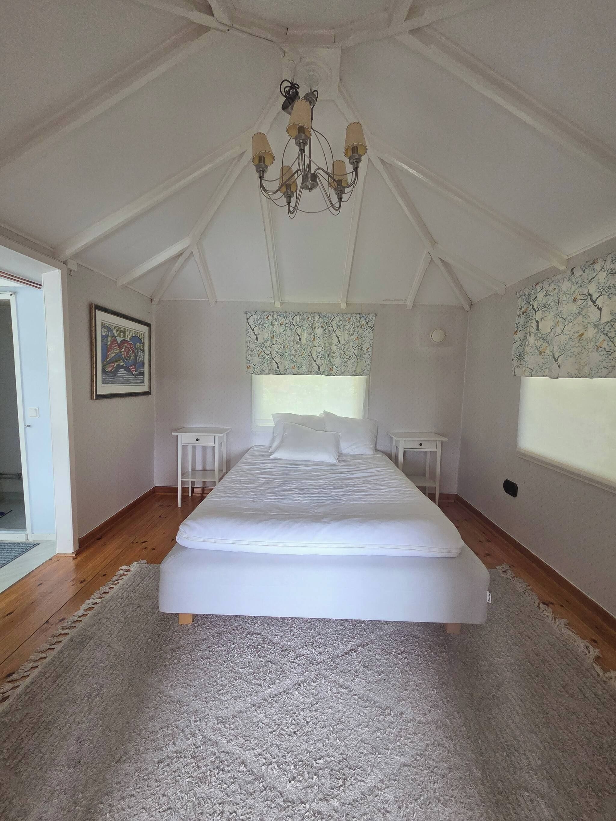A bedroom with a large bed, a chandelier, a window with a tree pattern curtain, and a door.