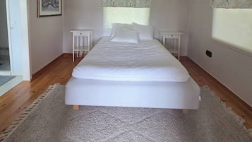 A bedroom with a large bed, a chandelier, a window with a tree pattern curtain, and a door.