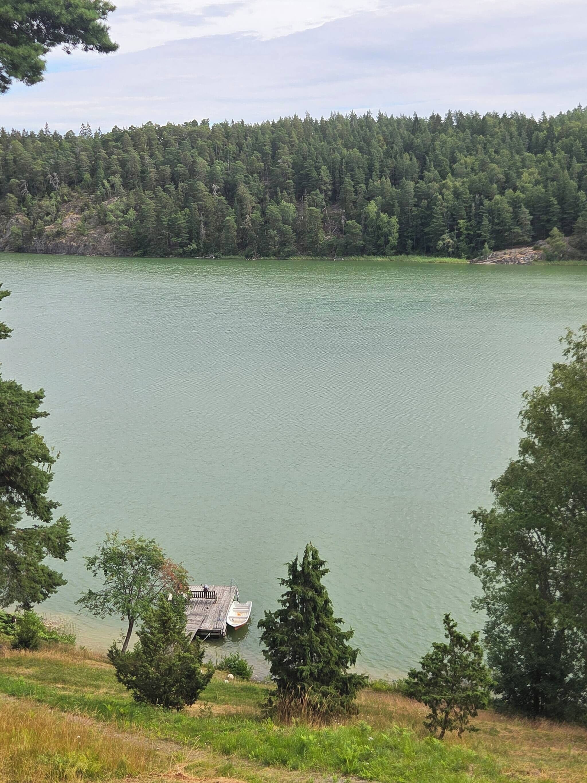 Un lac avec un quai et un petit bâtiment, le tout entouré d’une forêt dense.
