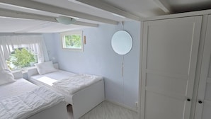 Un dormitorio con cama, armario, espejo redondo y ventana con cortinas.