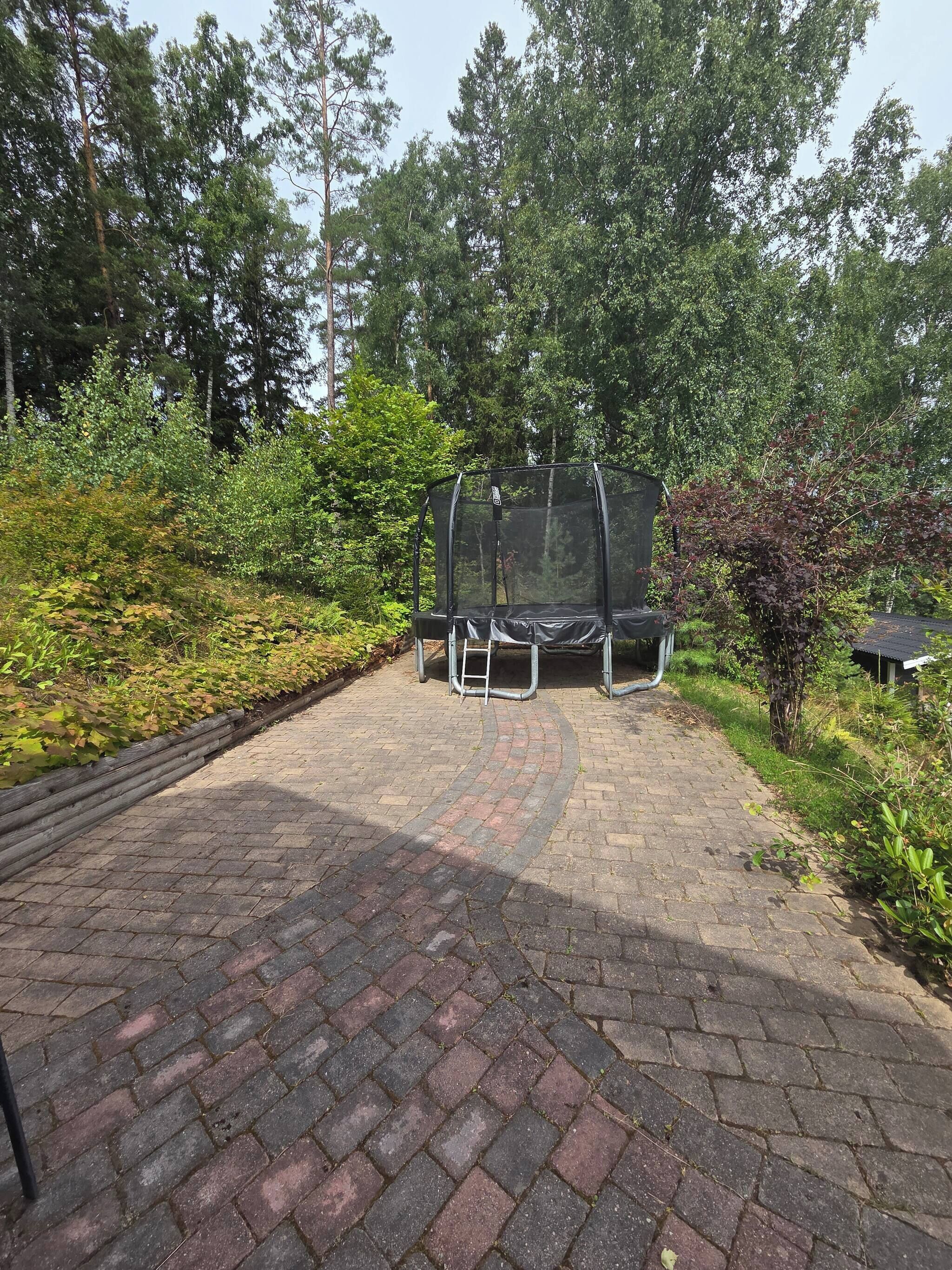 A paved outdoor area with a trampoline and a covered play structure.