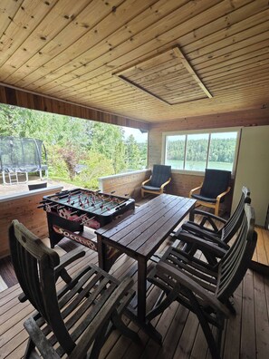 A wooden deck with a foosball table, chairs, and a view of a lake.