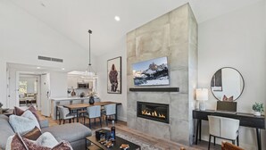 Ein modernes Wohnzimmer mit Kamin, Essbereich und einer Küche im Hintergrund.