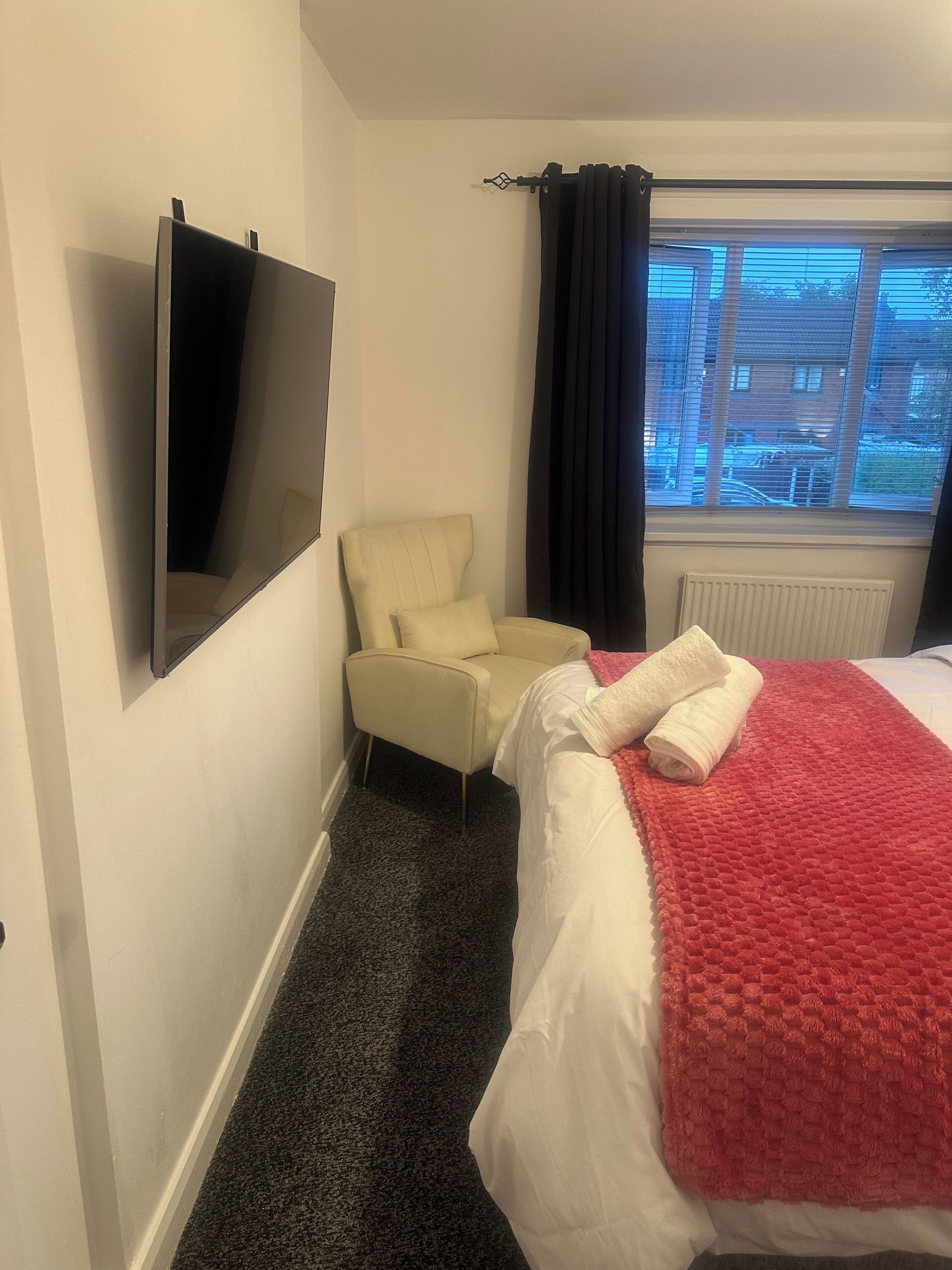 A hotel room with a bed, a chair, a TV mounted on the wall, and a window with curtains.