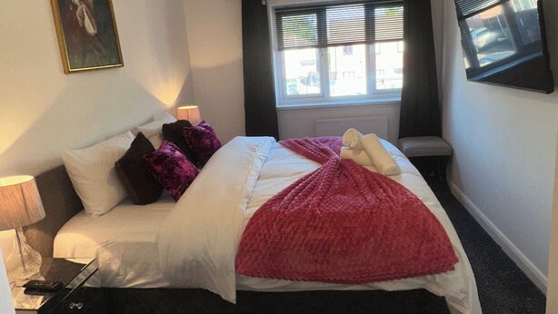 Un dormitorio con cama, mesita de noche, lámpara, ventana con cortinas, un cuadro en la pared y una lámpara del techo.