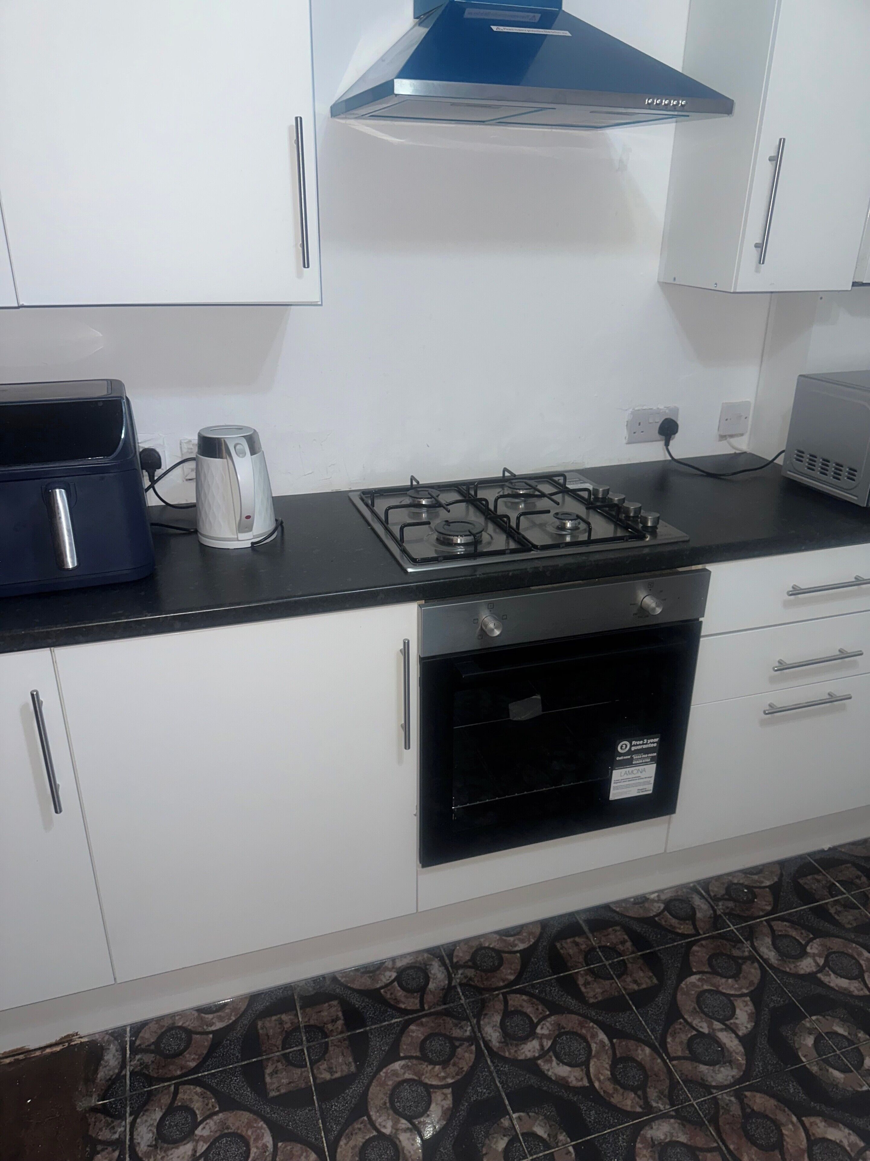 Cocina con gabinetes blancos, encimera negra, estufa a gas, hervidor y tostadora.
