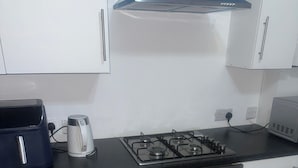 Cocina con gabinetes blancos, encimera negra, estufa a gas, hervidor y tostadora.