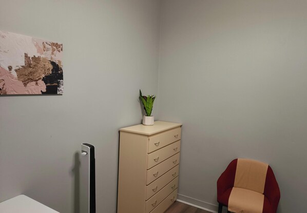 A room with a beige dresser, a red chair, a wall-mounted radiator, and a painting.
