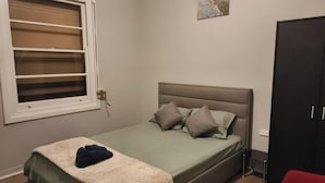 A bedroom with a bed, a window with blinds, a painting on the wall, and a wardrobe.