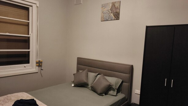 A bedroom with a bed, a window, a wall-mounted artwork, and a wardrobe.