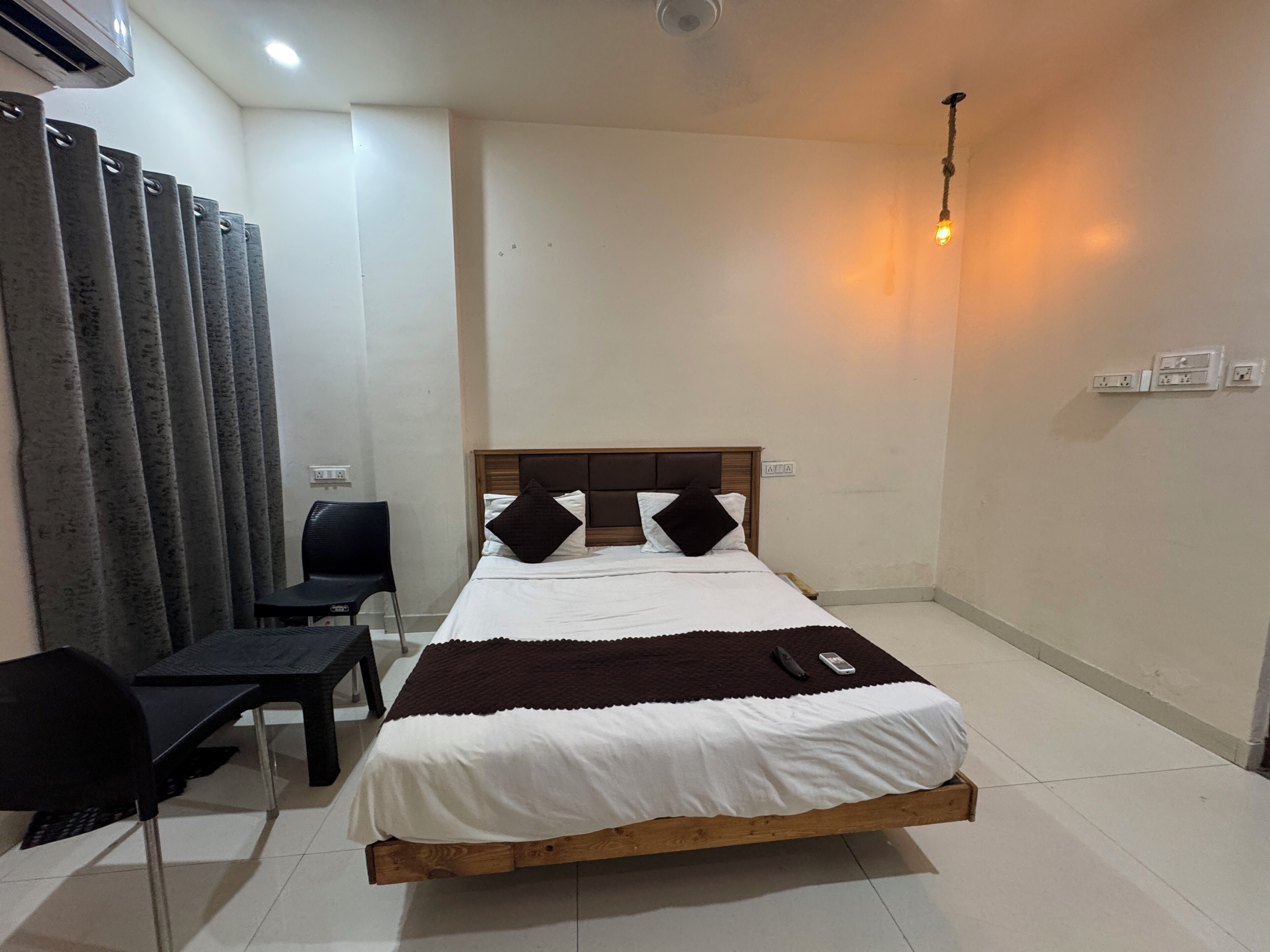 Una habitación de hotel con una cama individual, un escritorio, una silla y un ventilador de pie.