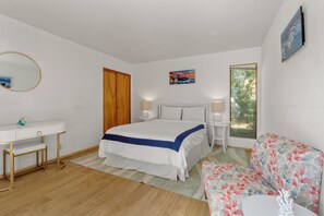 A bedroom with a bed, bedside tables, a desk, a chair, and a window with a view. - Seaclusion, by Vinifera Homes (Sea Ranch)