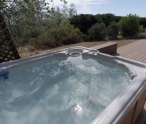 A hot tub with a wooden deck and surrounding vegetation. - Seaclusion, by Vinifera Homes (Sea Ranch)