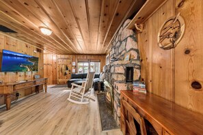 Interior acogedor de una cabaña con paredes de madera, una chimenea de piedra, un televisor y un sofá.