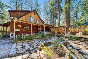 A wooden cabin with a porch, stone pathway, and a fenced garden area. - 3BR Tahoe Hideaway with Mountain Views and Rustic Feels (South Lake Tahoe)