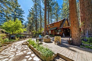 A rustic cabin with a stone patio, surrounded by tall trees and a garden area. - 3BR Tahoe Hideaway with Mountain Views and Rustic Feels (South Lake Tahoe)