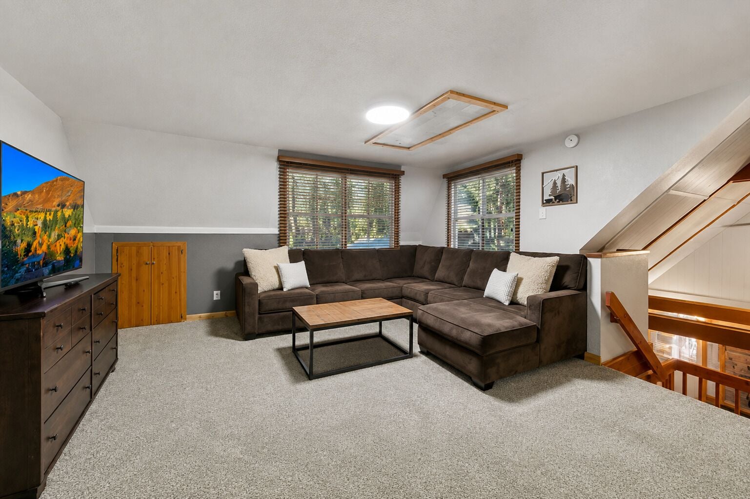 A living room with a sectional sofa, a coffee table, a TV on a wooden cabinet, and a staircase.