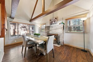 A dining area with a wooden table and chairs, a fireplace, and large windows with blinds. - Cozy Tahoe A-Frame Cabin - Minutes to Heavenly Ski Resort, Lake & Stateline | Pet Friendly (South Lake Tahoe)