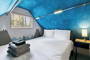 A bedroom with a bed, a window with blinds, a wall with a mountain design, and a bedside lamp. - Cozy Tahoe A-Frame Cabin - Minutes to Heavenly Ski Resort, Lake & Stateline | Pet Friendly (South Lake Tahoe)