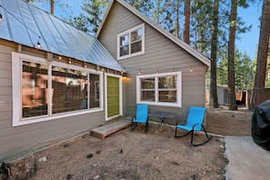 A small cabin with a metal roof, large windows, and a patio with two chairs. - Cozy Tahoe A-Frame Cabin - Minutes to Heavenly Ski Resort, Lake & Stateline | Pet Friendly (South Lake Tahoe)