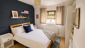 Un dormitorio con cama, mesitas de noche, radiador, ventana con cortinas y adornos en la pared.