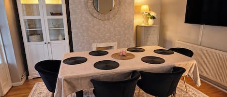 Un comedor con una mesa, sillas, un armario, un espejo, una lámpara y un televisor en la pared.
