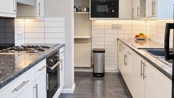 A modern kitchen with white cabinets, a stainless steel range, a microwave, and a black refrigerator.
