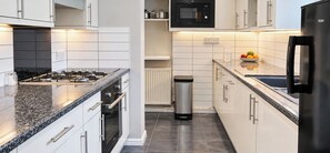 A modern kitchen with white cabinets, a stainless steel range, a microwave, and a black refrigerator. - 3-bed Hot Tub Pool Table Off-road Parking Sleeps 5 (Birmingham)