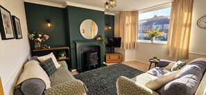 A living room with a fireplace, a television, and a window with curtains. - 3-bed Hot Tub Pool Table Off-road Parking Sleeps 5 (Birmingham)
