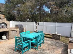 Eine Terrasse im Freien mit einem Ziegelofen, Grill und einem türkisfarbenen Tisch und Stühlen.