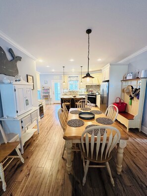 A spacious kitchen with a central island, wooden dining table, and white chairs. - Brisas del Mar- a West End Retreat, 6 BR, Dual Living spaces, 6 Seater Golf Cart (Oak Island)