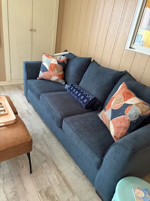 Ein Zimmer mit einem dunkelblauen Sofa, einem braunen Hocker und einem türkisfarbenen Schemel.