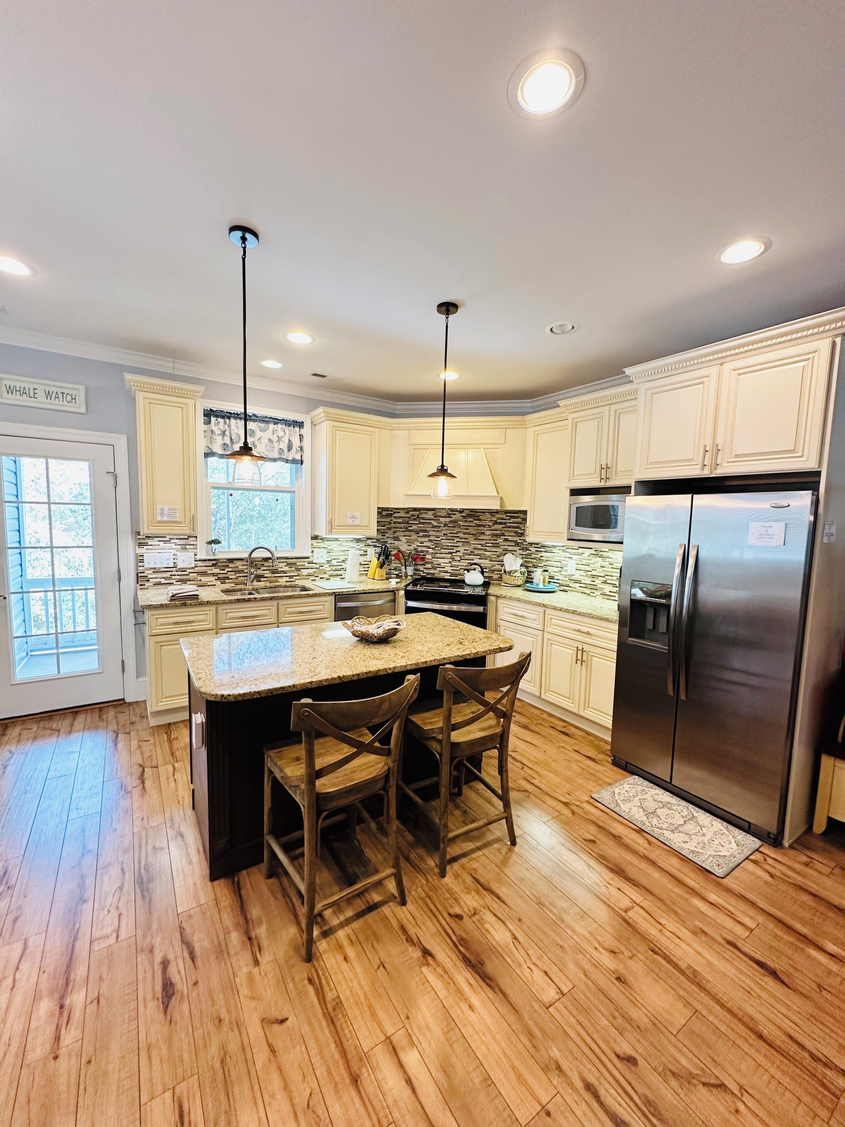 A kitchen with a central island, wooden flooring, and a stainless steel refrigerator.