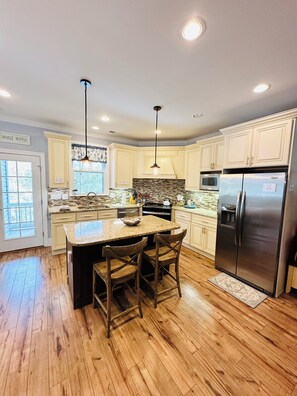 A kitchen with a central island, wooden flooring, and a stainless steel refrigerator. - Brisas del Mar- a West End Retreat, 6 BR, Dual Living spaces, 6 Seater Golf Cart (Oak Island)