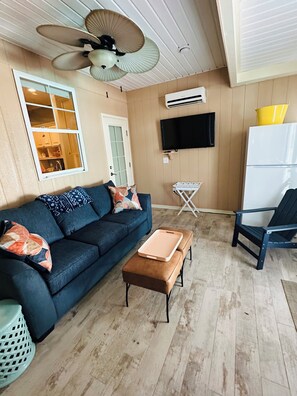 Ein Wohnzimmer mit einer Couch, einem Hocker und einem an der Wand befestigten Fernseher.